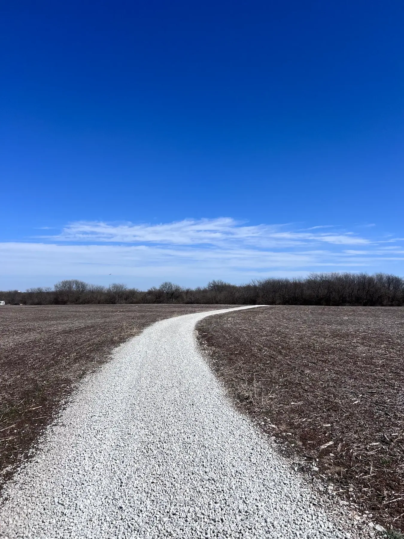 Freshly built rock driveway crossing an open field under a blue sky