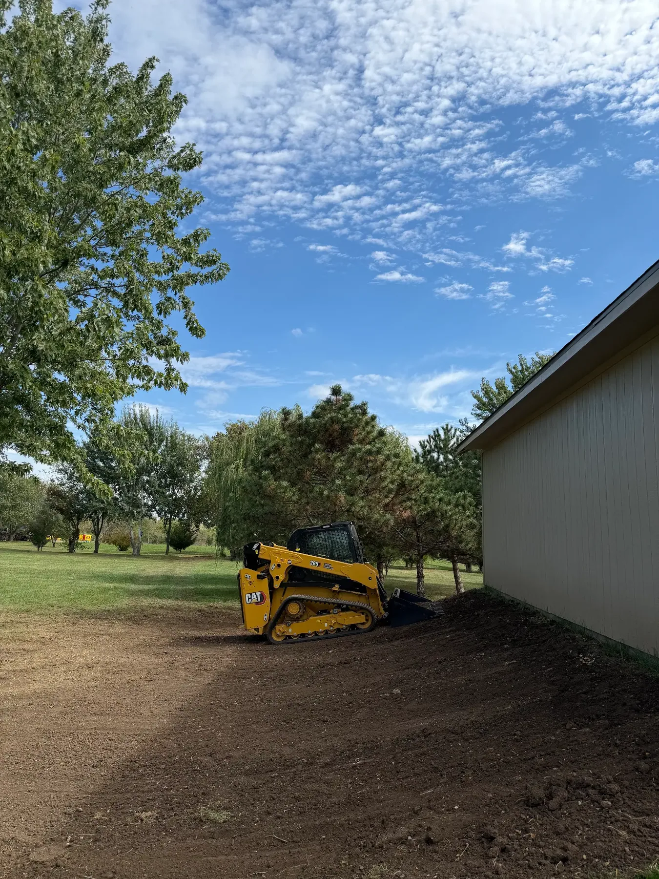 CAT track loader shaping and grading dark soil beside a new outbuilding