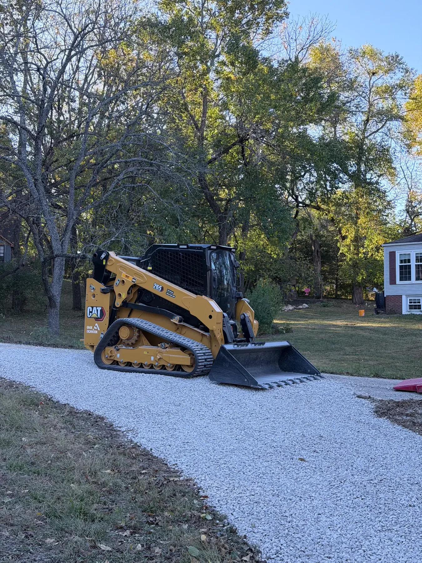 CAT track loader on a finished white rock driveway beside a home