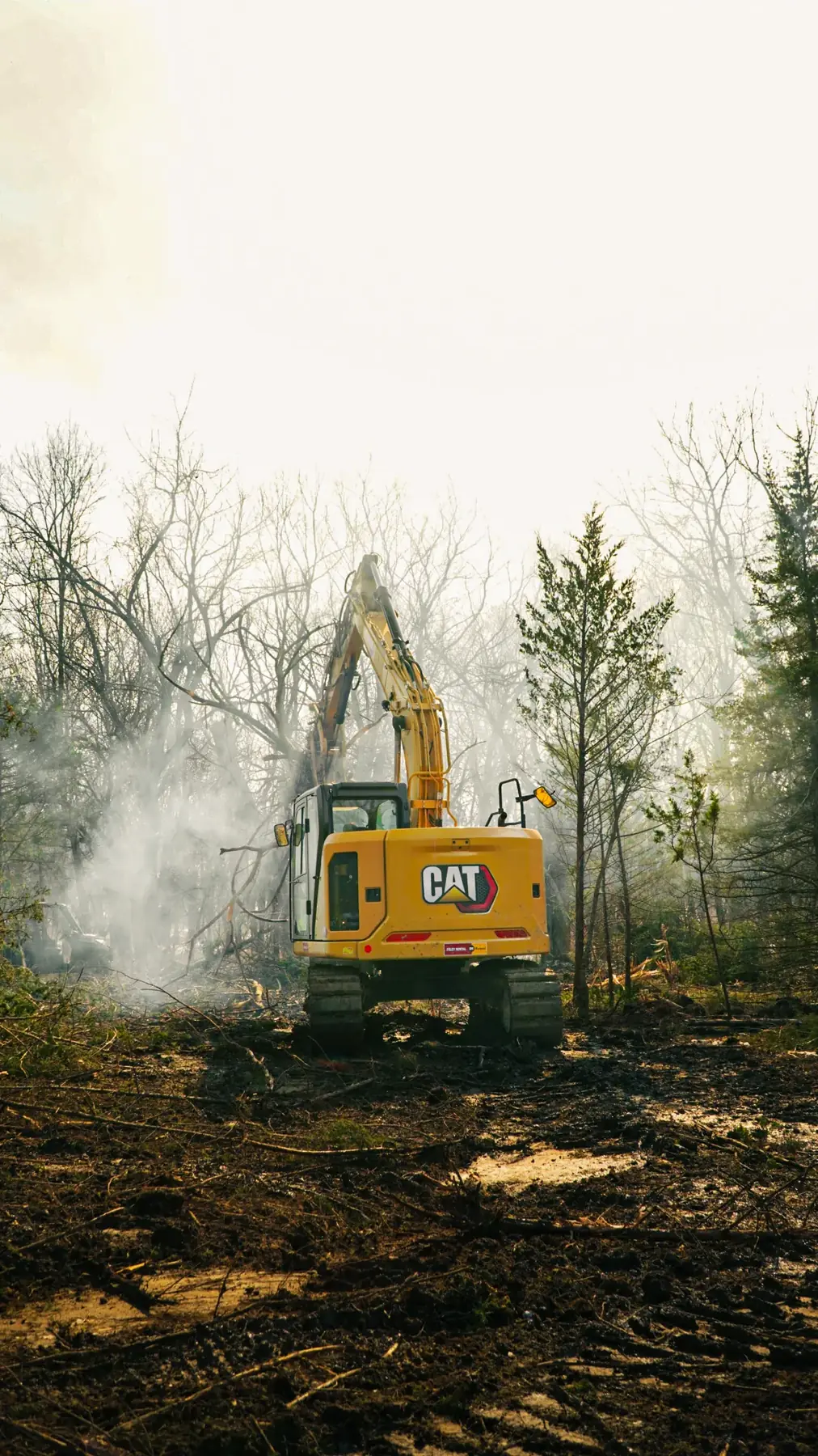 CAT excavator pulling down trees in the haze on a muddy clearing job