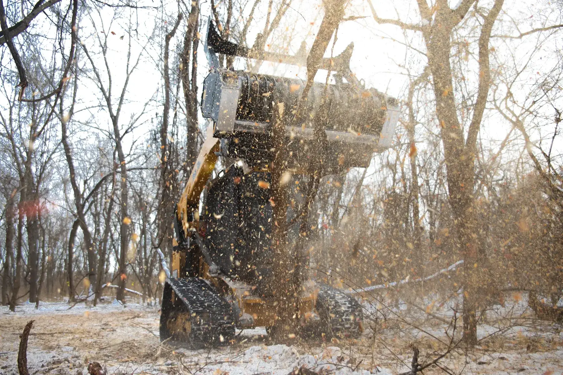 Wood chips flying from a drum mulcher head during forestry mulching