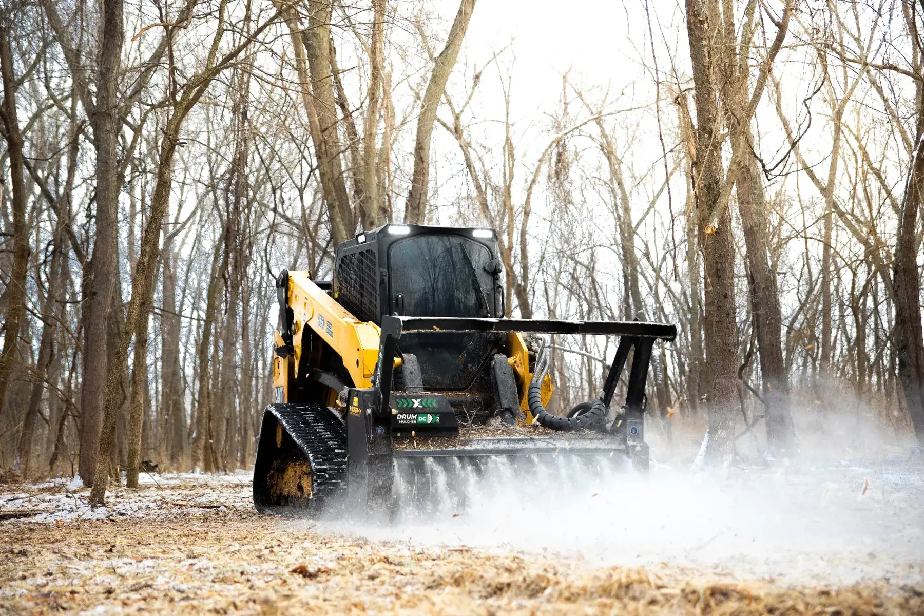 CAT 265 track loader mulching brush and saplings across a snowy Kansas woodlot
