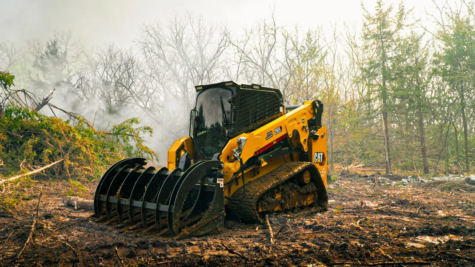 CAT 265 track loader with a grapple in a smoky land clearing site