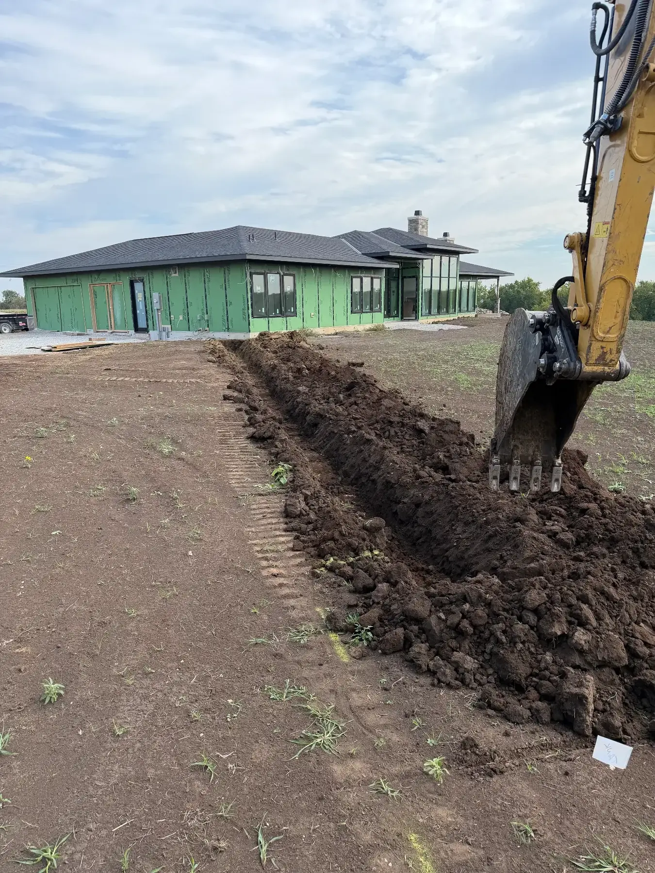 Excavator cutting a long trench beside a new home under construction