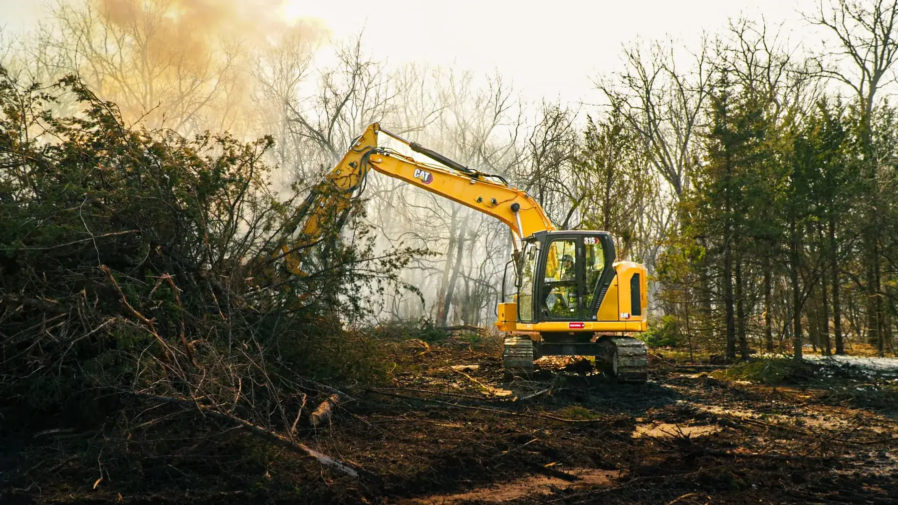 CAT excavator stacking cleared trees and brush into a pile on a Kansas clearing job