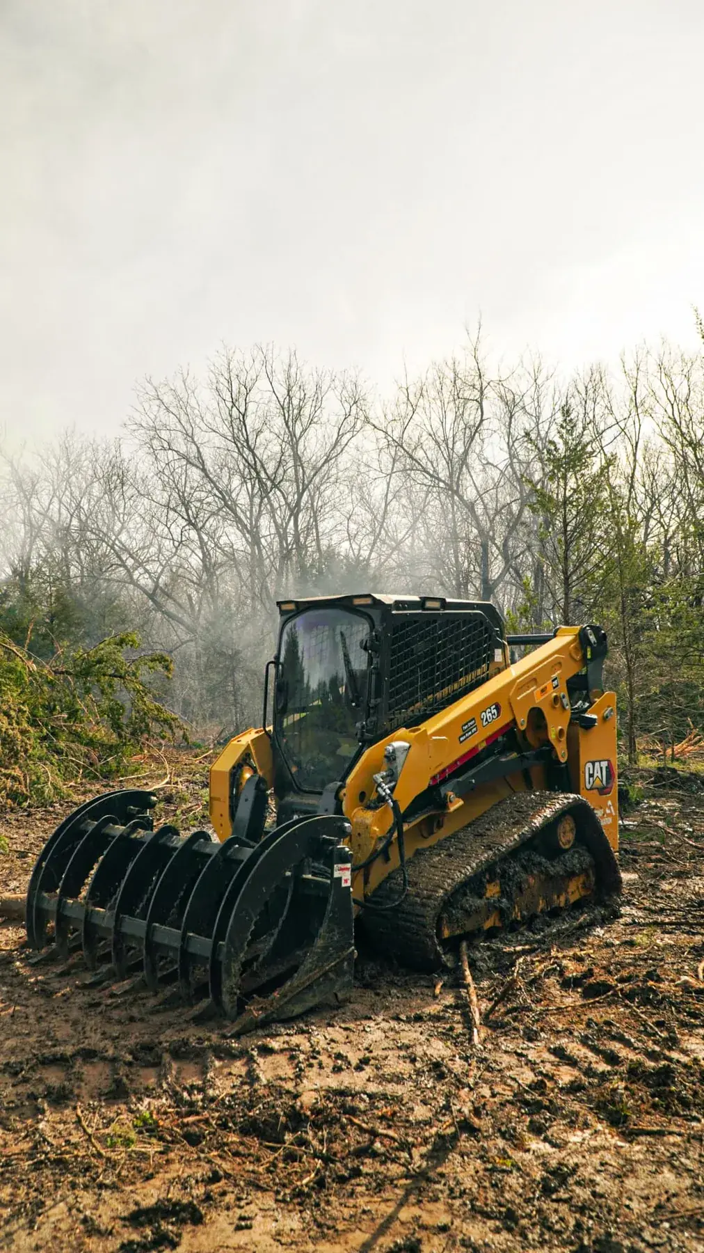 CAT 265 track loader with a grapple attachment stacking cleared brush in the woods